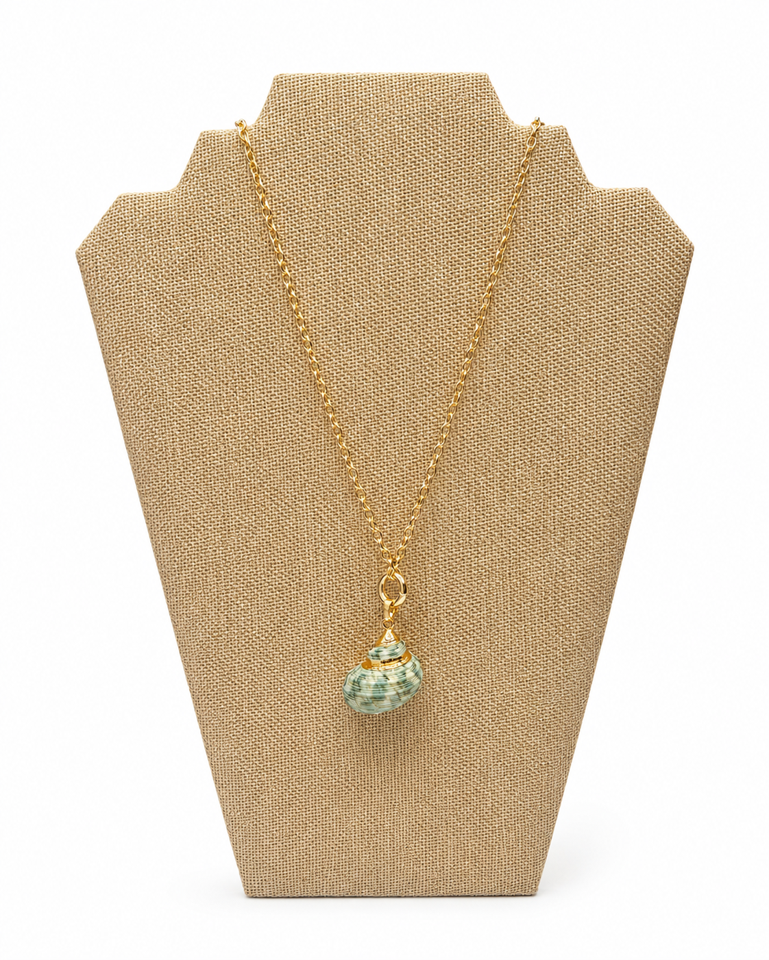 A gold chain necklace with a small green shell pendant, displayed on a textured beige jewelry bust against a white background.
