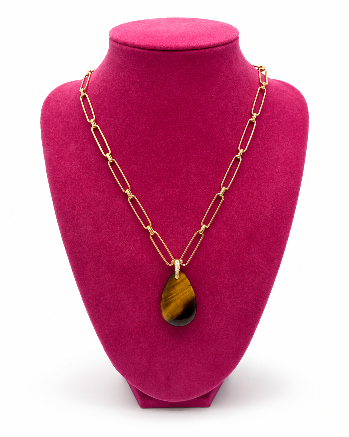 A gold chain necklace with a teardrop-shaped tiger's eye pendant, displayed on a bright magenta jewelry bust against a white background.