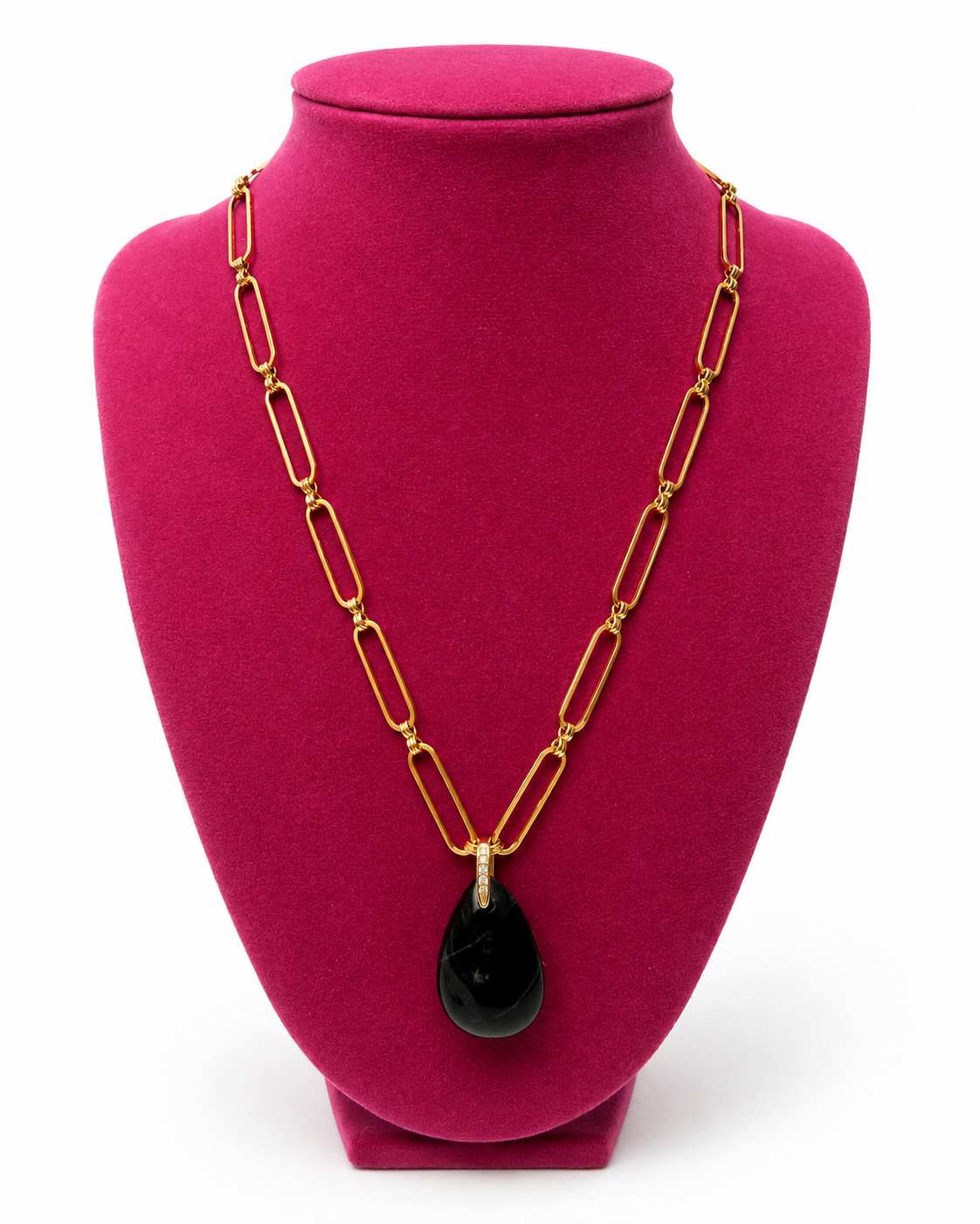 A gold paperclip chain necklace with a black teardrop pendant, displayed on a magenta jewelry bust against a white background.